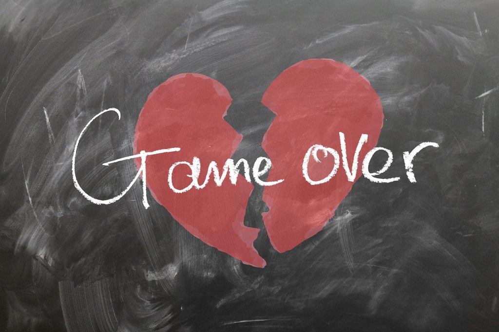 Corazón rojo roto con la frase 'Game Over' escrita sobre una pizarra, simbolizando el final de una relación amorosa o la ruptura de un vínculo emocional.
